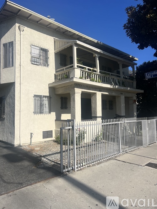 A white two-story building with a balcony and a metal fence in front.