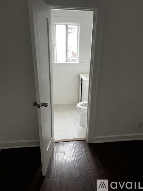 A white door is open to a bathroom with a toilet and a window.