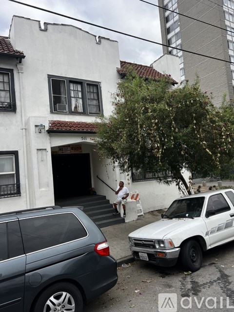 A white car is parked on the street in front of a white building with a black gate.