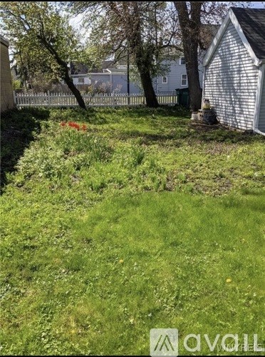 A grassy area with a white house and a shed in the background.