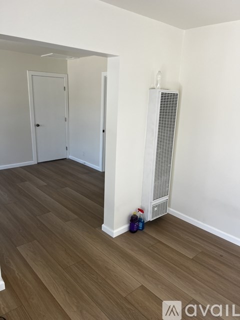 A room with a white wall and a wooden floor with a radiator and a bottle.