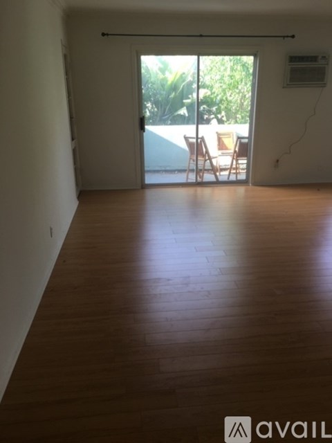 A room with wooden flooring and a sliding glass door leading to a balcony.