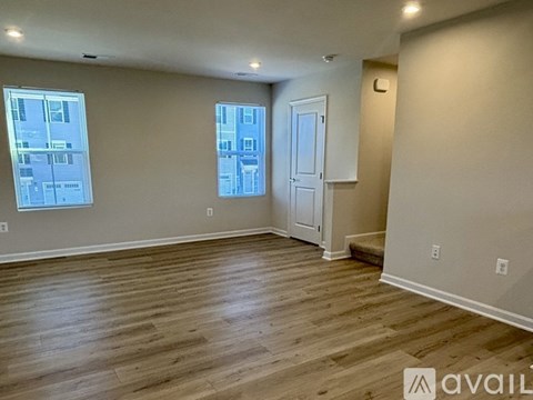 A room with wooden flooring and two windows.