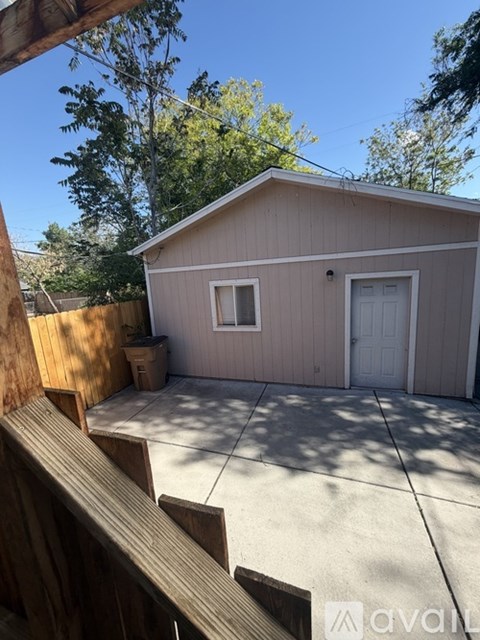 A small building with a white door and windows is surrounded by a wooden fence.