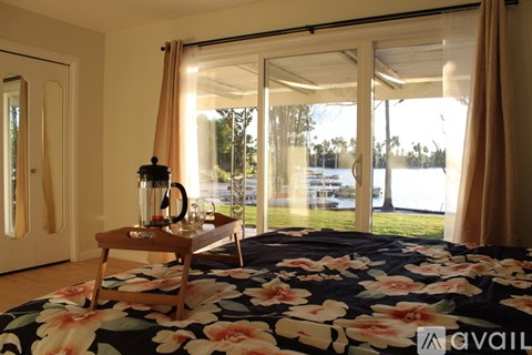 A bedroom with a bed, a table with a blender on it, and a window with curtains.