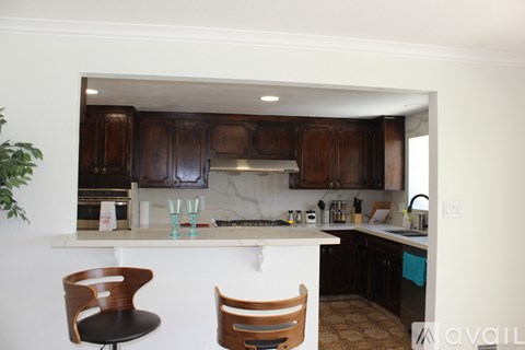 A kitchen with a white counter top and wooden chairs.