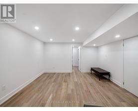 A room with wooden flooring and white walls, with a bench and a door visible.