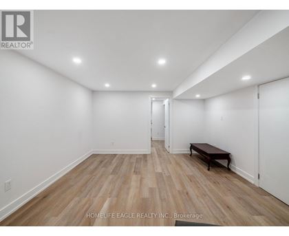 A room with wooden flooring and white walls, with a bench and a door visible.