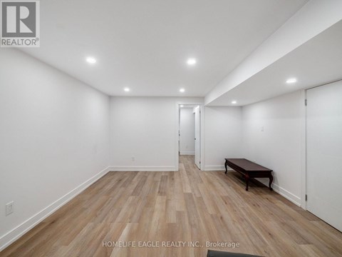 A room with wooden flooring and white walls, with a bench and a door visible.