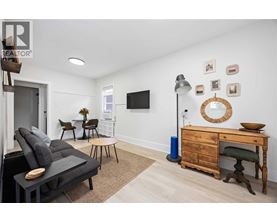 A living room with a grey sofa, a wooden desk, and a TV mounted on the wall.