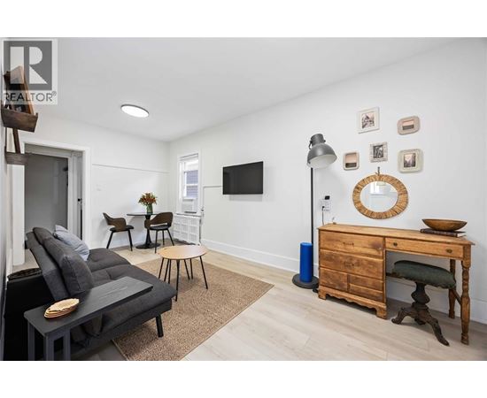 A living room with a grey sofa, a wooden desk, and a TV mounted on the wall.