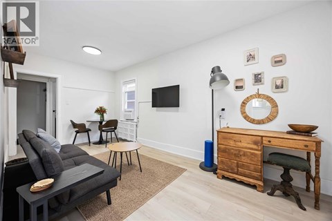 A living room with a grey sofa, a wooden desk, and a TV mounted on the wall.