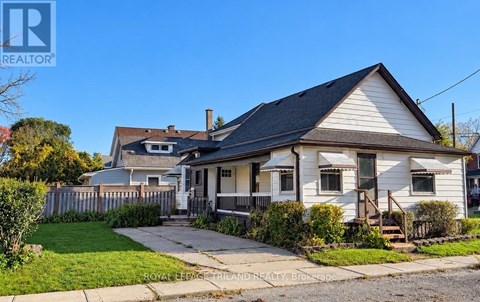 A white house with a brown roof is surrounded by a green lawn and a wooden fence.