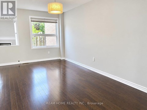 A room with wooden floors and a window showing a view of a backyard.