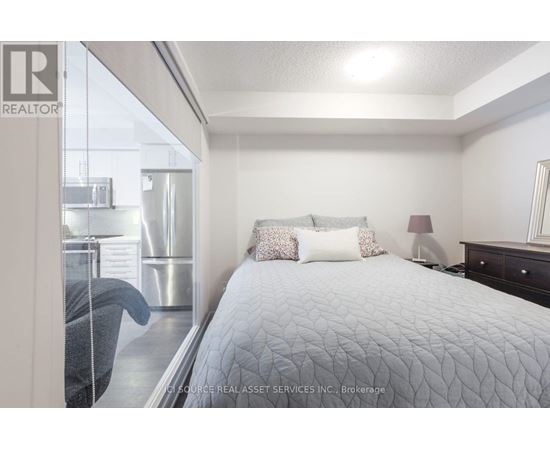 A bedroom with a large bed and a window overlooking a kitchen.