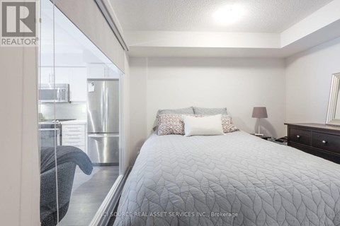 A bedroom with a large bed and a window overlooking a kitchen.