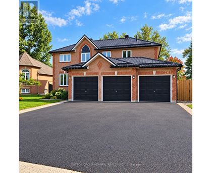 A house with a brick facade and a black roof has a driveway in front.