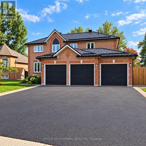 A house with a brick facade and a black roof has a driveway in front.