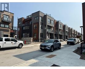 A row of modern townhouses with cars parked in front.