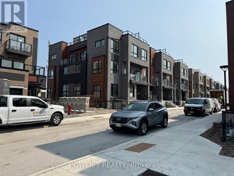 A row of modern townhouses with cars parked in front.