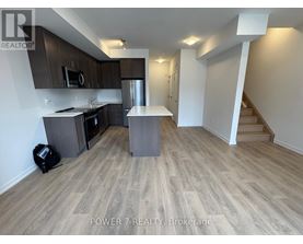 A kitchen with wooden flooring and a staircase in the background.