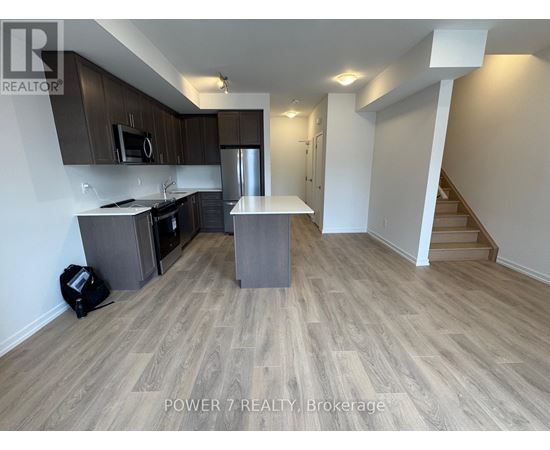 A kitchen with wooden flooring and a staircase in the background.