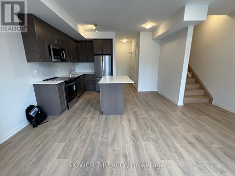 A kitchen with wooden flooring and a staircase in the background.