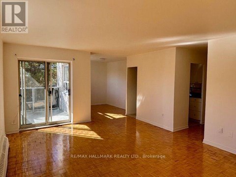 A spacious room with a wooden floor and white walls, with a sliding glass door leading outside.