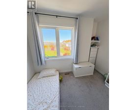A bedroom with a bed, a window with a view of a garden, and a white cabinet.