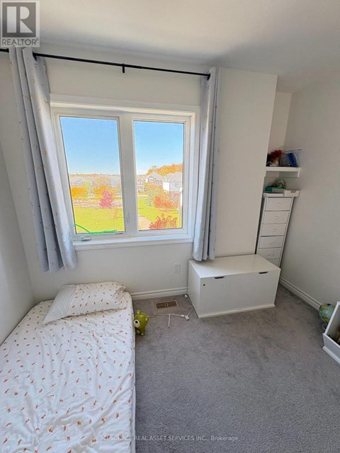 A bedroom with a bed, a window with a view of a garden, and a white cabinet.