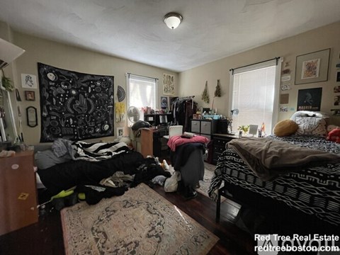 A messy bedroom with a bed, dresser, and a rug.