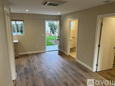 A spacious room with wooden flooring and a view of a green lawn through a glass door.