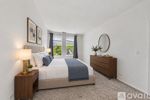 A bedroom with a bed, nightstand, and a round mirror on the wall.