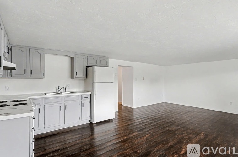 A kitchen with white appliances and cabinets with a wooden floor.