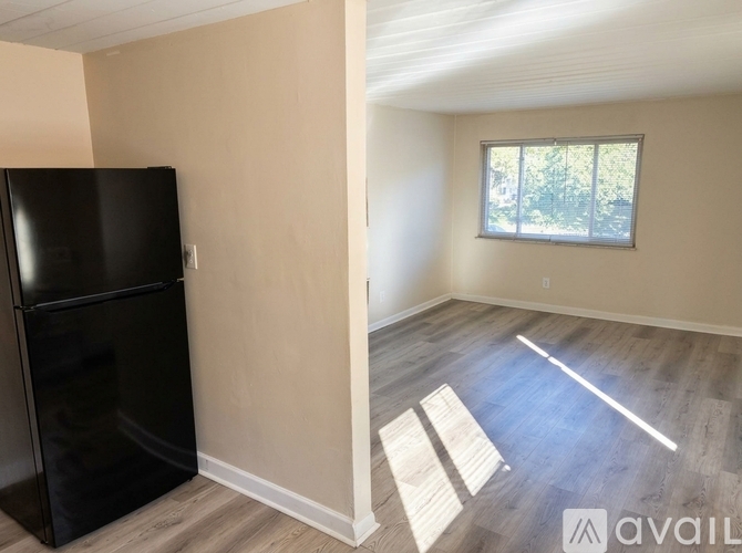 A black fridge sits in a room with wooden floors and a window.