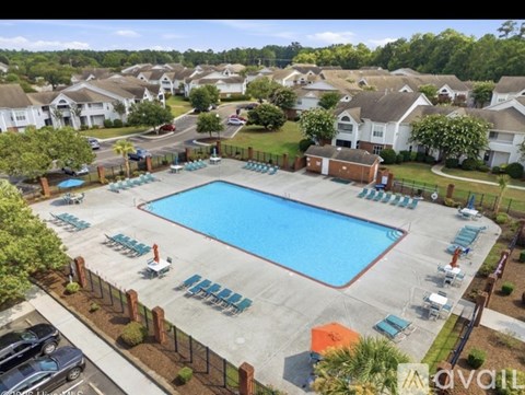 A large swimming pool surrounded by a fence and lounge chairs.