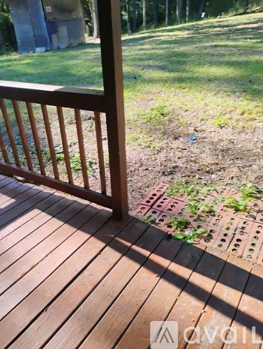 A wooden deck with a railing and a brick pathway leading to a grassy area.