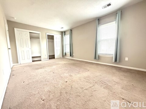 A sparsely furnished room with a carpeted floor and a window with blinds.