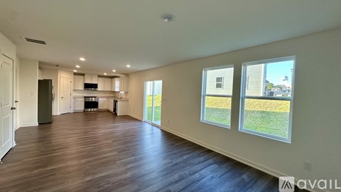 A spacious living room with hardwood floors and a kitchen area in the background.