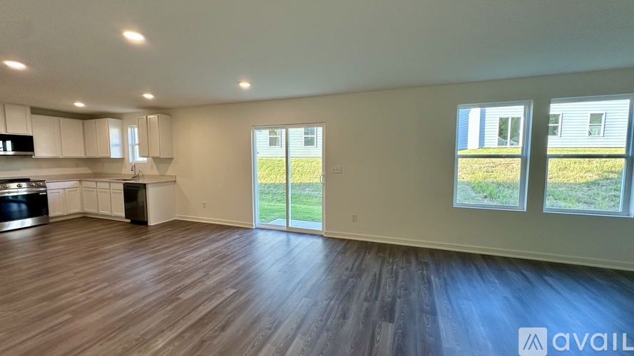 A spacious room with wooden flooring and a kitchen area with white cabinets and appliances.