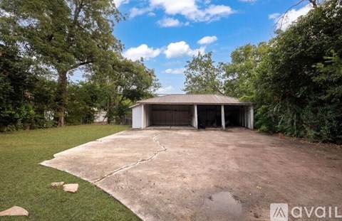 A large, open garage with a concrete floor and a metal roof is surrounded by greenery.