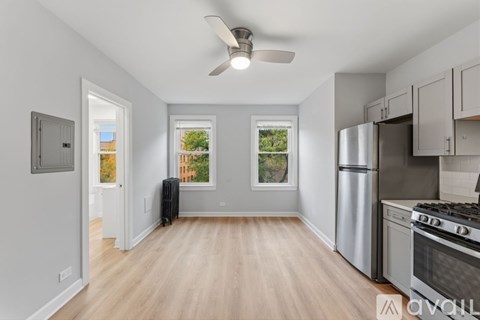 A kitchen with a stainless steel refrigerator and stove, wooden flooring, and a ceiling fan.