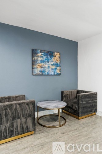 A living room with a grey couch, a round table and a painting on the wall.