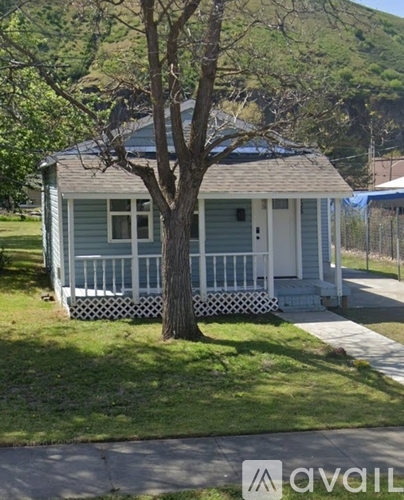 A small house with a porch and a tree in front.