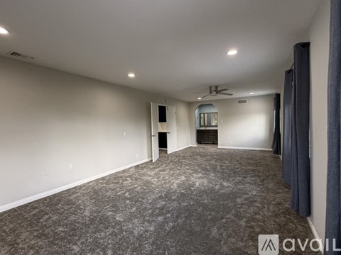 A spacious room with a grey carpet and a ceiling fan.