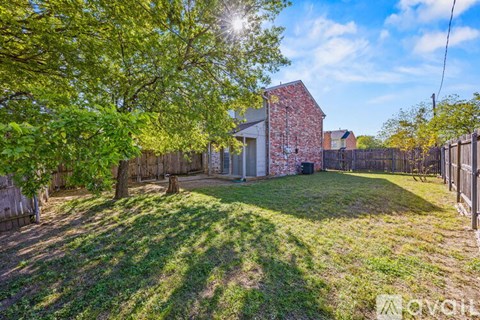A backyard with a tree, a fence and a house.
