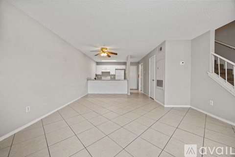 A spacious room with a ceiling fan and a kitchen area in the background.