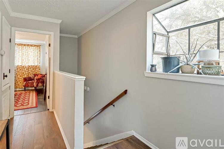 A hallway with a wooden staircase and a window with a view of trees outside.