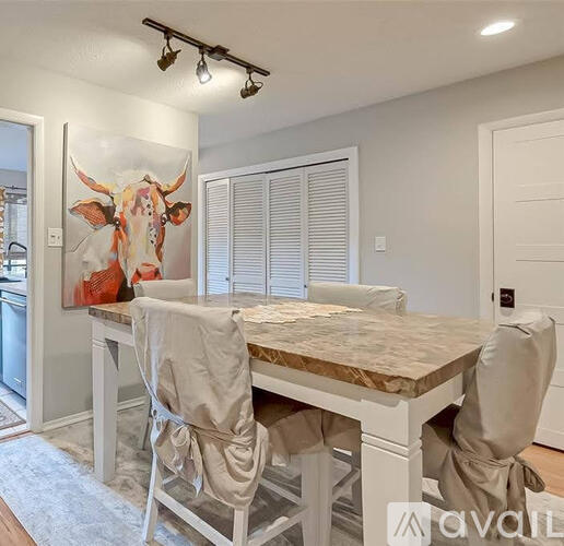A dining room with a table and chairs and a painting of a cow on the wall.
