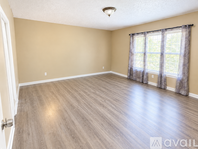 A spacious room with wooden flooring and a window with curtains.